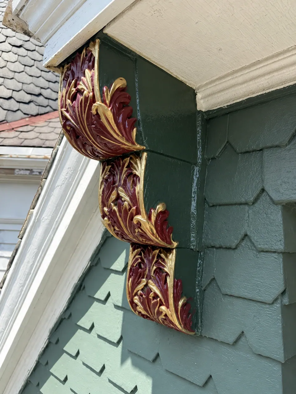 A rendering of the same bracket painted: deep green sides, and the carved acanthus leaves in burgundy with gold edges, under the cream eave.